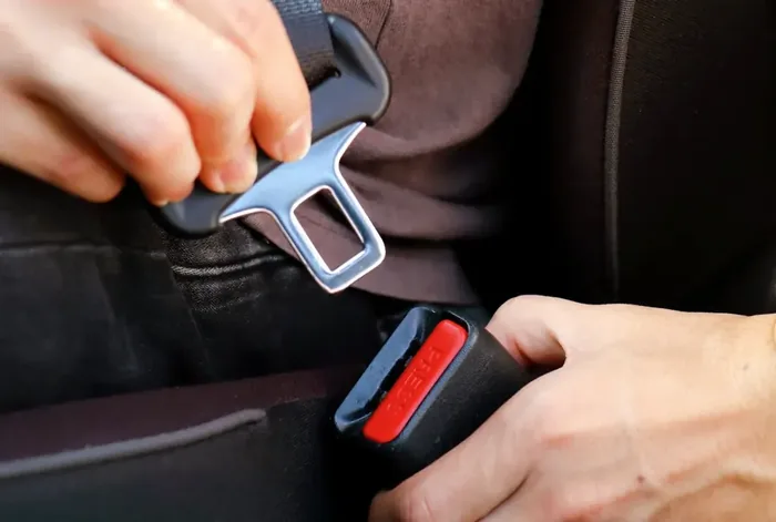Hands guiding a seat belt latch plate into the buckle receiver.
