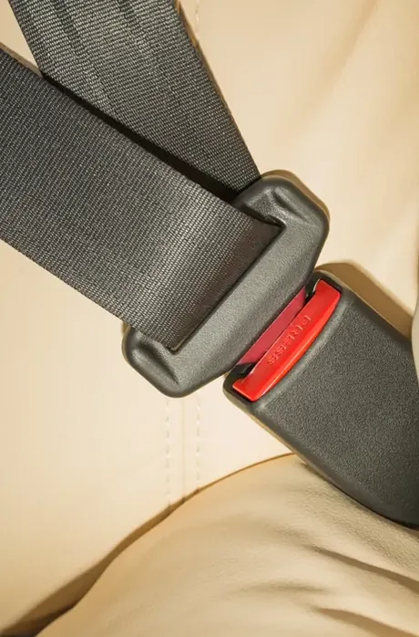 Seat belt fastened across a light-coloured vehicle seat, buckle and webbing in view.