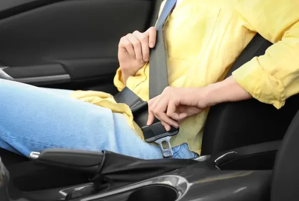 Person fastening a seat belt in a car, the webbing and buckle visible in detail.