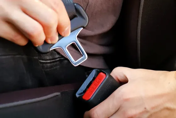 Hands guiding a seat belt latch plate into the buckle receiver.