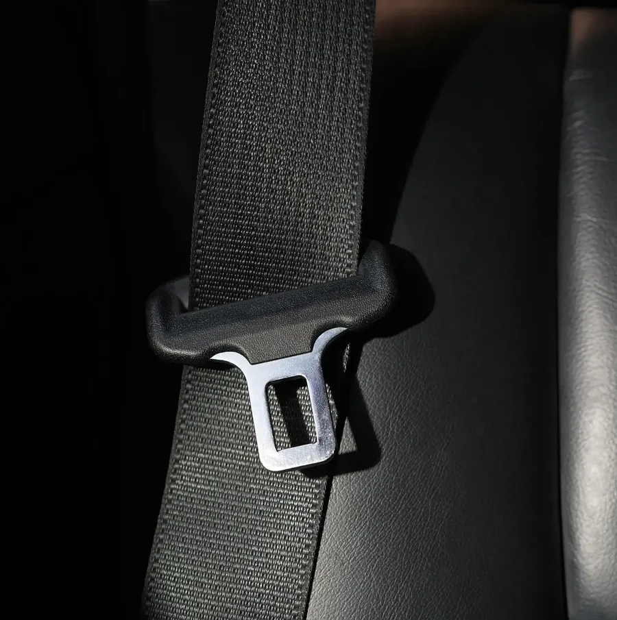 Seat belt webbing threaded through a metal latch plate, photographed close up in low light.