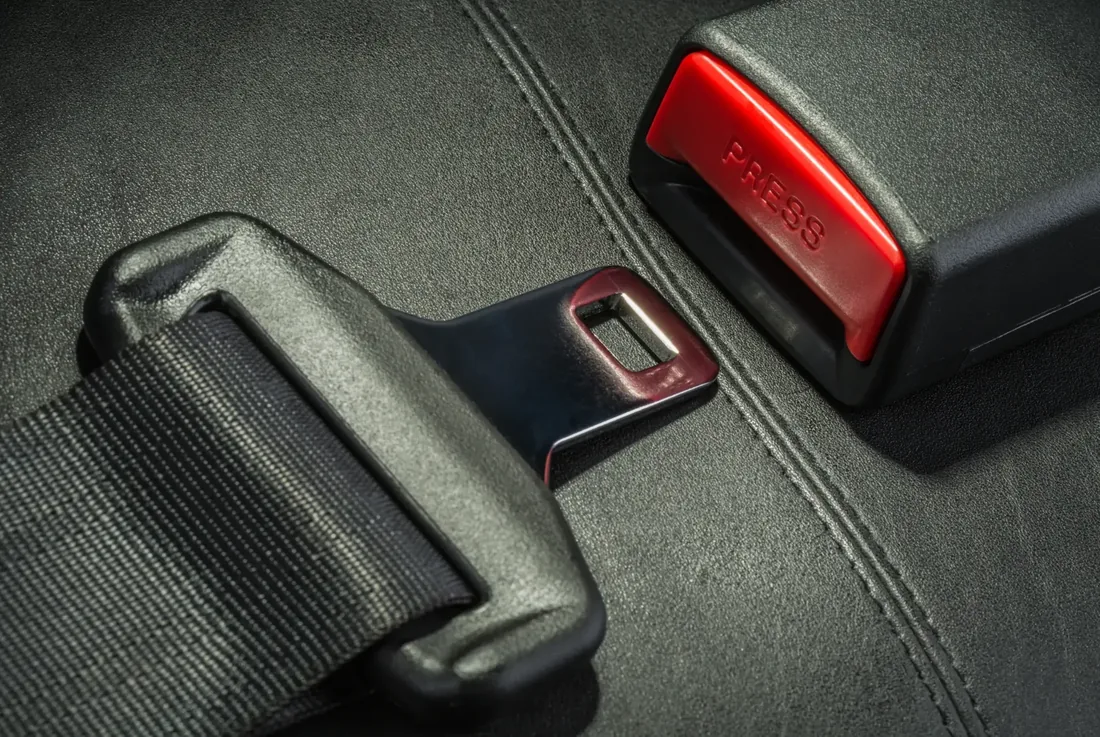 Close-up of a fastened automotive seat belt: the latch plate seated in the buckle receiver beside the red release button.