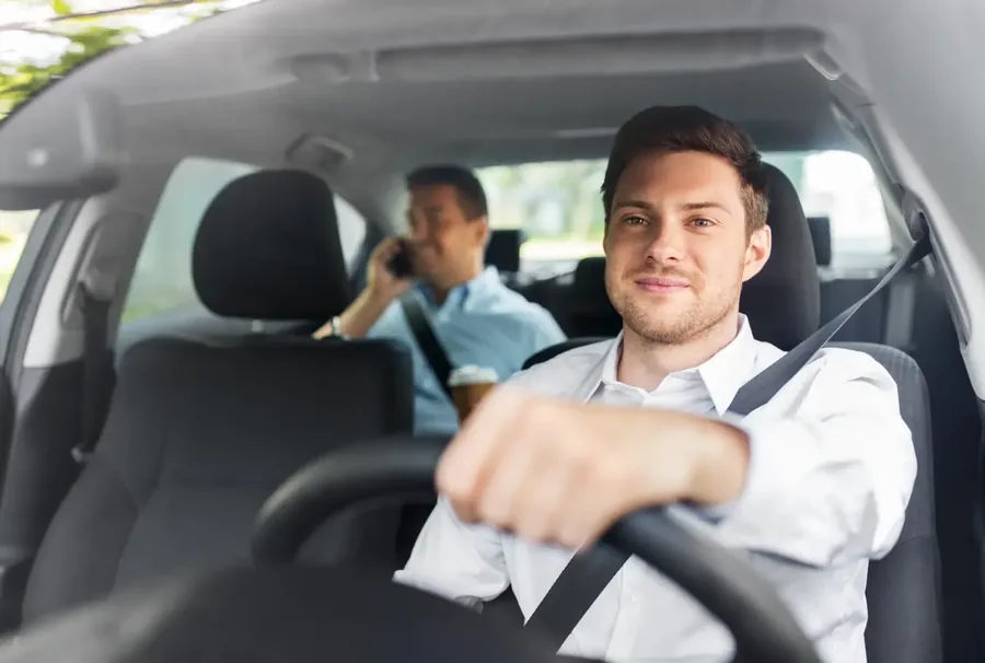 Driver and rear passenger seated in a car with seat belts fastened across the chest and lap.