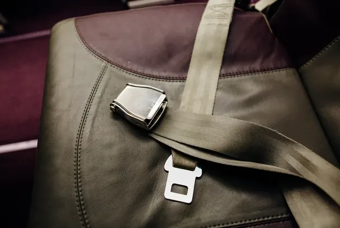 Lap belt with a metal lift-latch buckle resting across an olive-toned vehicle seat.