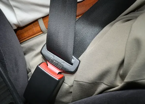 Seat belt buckled at the hip of a seated occupant, showing the latch plate and buckle in use.