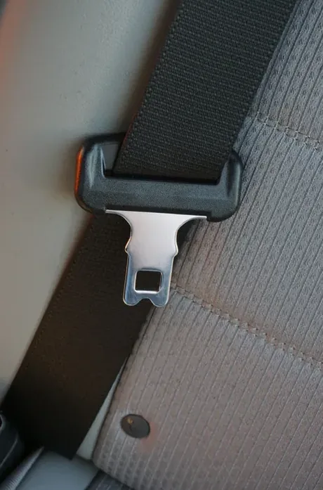 Seat belt webbing and latch plate resting on a grey fabric vehicle seat.
